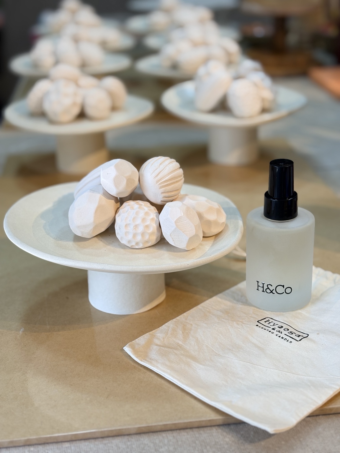 Scent Rocks de cerâmica clara sobre prato alto, ao lado de frasco Hyooga & Co. e saquinho de algodão com a marca