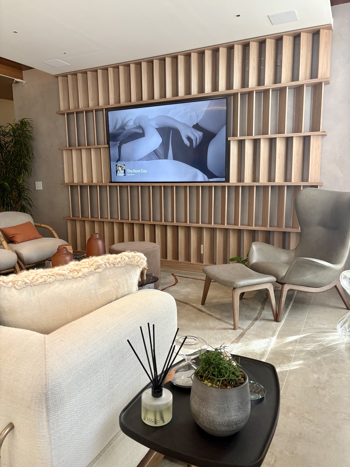 Difusor Hyooga & Co. com varetas pretas sobre mesa lateral de sala de estar, ao lado de vaso com planta e poltronas claras